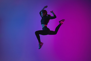 Fototapeta na wymiar Fit sporty woman jumping in studio against phantom blue color background. Young beautiful girl in jumping moment