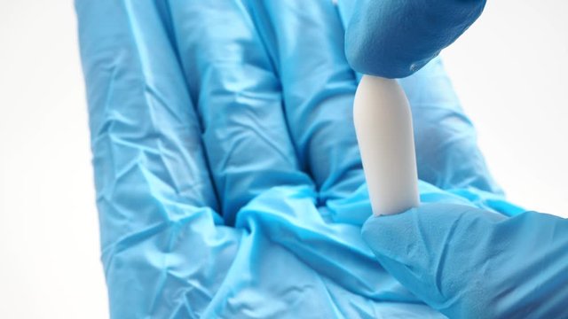 White suppository for anal or vaginal use in hands of doctor wearing blue gloves. Medical candles for treatment of Candida, thrush, hemorrhoids, inflammation and fever. Effective drug close up