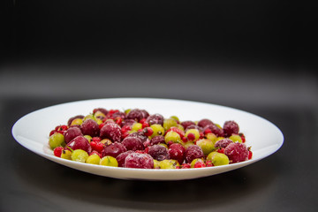 Frozen berries from the freezer. Plate with frozen cherries, currants and gooseberries. Healthy berry on a white plate.
