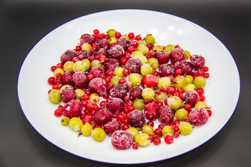 Frozen berries from the freezer. Plate with frozen cherries, currants and gooseberries. Healthy berry on a white plate.