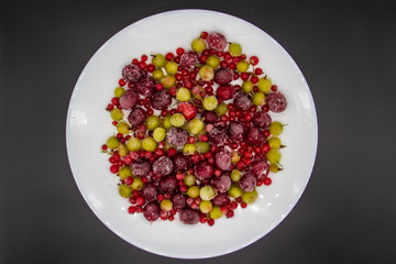 Frozen berries from the freezer. Plate with frozen cherries, currants and gooseberries. Healthy berry on a white plate.