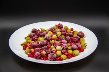 Frozen berries from the freezer. Plate with frozen cherries, currants and gooseberries. Healthy berry on a white plate.