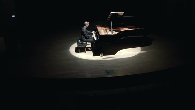 Grand Piano On Stage : An elegant man in a black suit playing grand piano on stage in a concert hall, aerial video