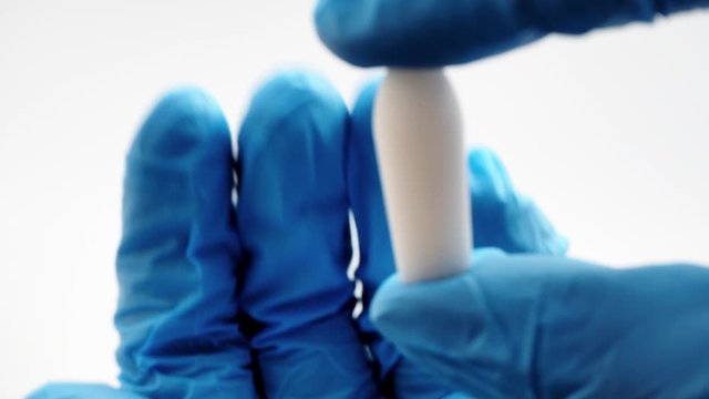 White suppository for anal or vaginal use in hands of doctor wearing blue gloves. Medical candles for treatment of Candida, thrush, hemorrhoids, inflammation and fever. Effective drug close up