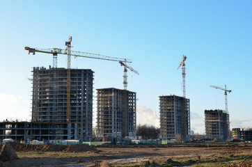 Tower cranes constructing a new residential building at a construction site against blue sky. Renovation program, development, concept of the buildings industry.