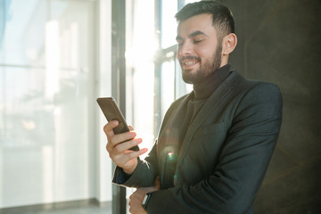 Happy young businessman scrolling in smartphone and looking through contacts