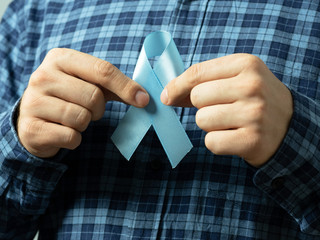 A man in a plaid shirt holds two hands blue Ribbon symbol of prostate cancer awareness.Concept of...