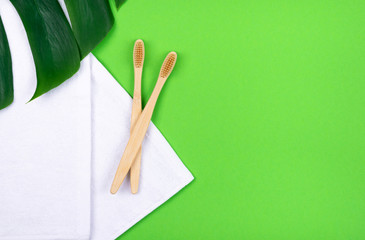 Two bamboo toothbrushes on towels on green background and tropical plant leaf monstera . Plastic free concept.
