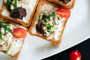 Brushetta set. Variety of small sandwiches with egg, tuna, arugula and salad served with glass of cognac on a black stone board over dark background
