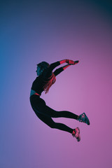 Sporty charismatic woman jumping against colorful trendy color. Young athletic girl in jump moment in studio
