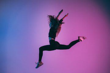 Fototapeta na wymiar Fit sporty woman jumping in studio against phantom blue color background. Young handsome girl in jumping moment
