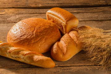 Bread and wheat ears on wooden background. Various types of freshly baked bread with wheat ears on rustic wooden table.