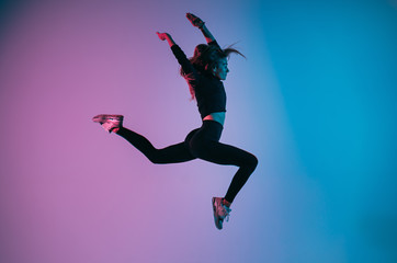 Fototapeta na wymiar Sporty girl in charismatic jump moment against trendy color background. Young fit dance woman jumping. Studio shot