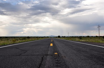 straight asphalt road with yellow markings and a power line side. Mountain on the background.