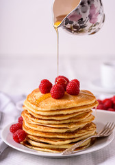 Sweet homemade pancakes with raspberries on white plate with fork.