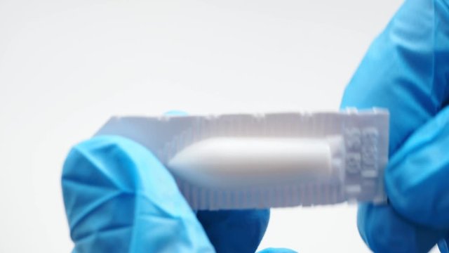 White suppository for anal or vaginal use in hands of doctor wearing blue gloves. Medical candles for treatment of Candida, thrush, hemorrhoids, inflammation and fever. Effective drug close up
