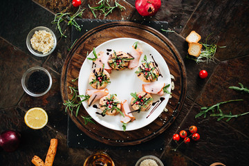 Cheese rolls in ham with donuts with arugula under pomegranate sauce and dark background