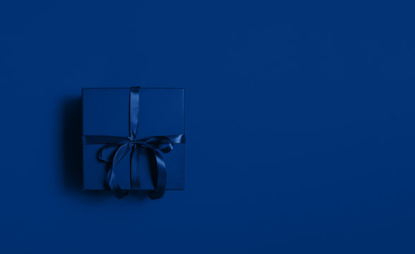 Blue gift box with bow on classic blue paper backround. Flat lay, top view