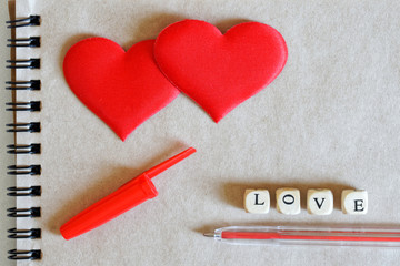 Two red silk hearts with a fountain pen and notepad made of ecological paper. Non-standard, catchy word love with an inverted letter. Blank for inscriptions. Happy Valentine's Day Greeting Card.