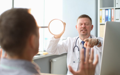 Angry doctor interrogates the patient, yelling at him, pointing to man he talking to and holding lamp base.