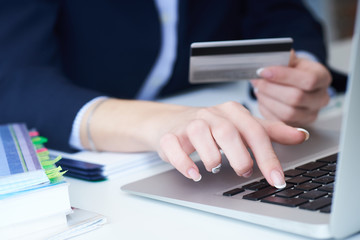 Fototapeta premium Businesswoman inputting her password and login to carry out online banking operation on laptop pc in the office. Woman's hand holding credit card close-up.