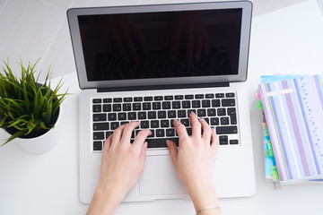 Businesswoman sitting at office desk and typing on a laptop hands close up. View from above.