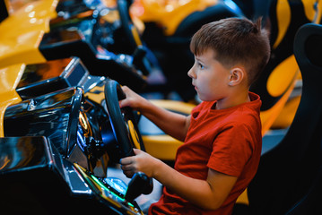 Happy European boy playing racing simulator at indoor playground.