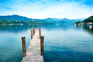 Wooden pier on Orta San Giulio Lake with greenery mountain background. Italy.