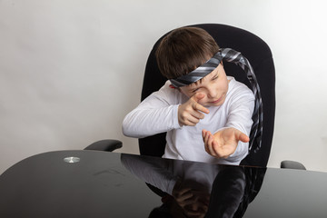 The boy plays, imagines that he is a hunter. Sits at the desk. In a white T-shirt, a man’s tie on his head.