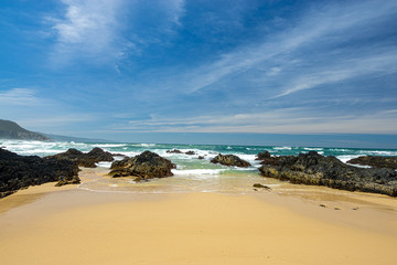 Fototapeta na wymiar Sandstrand mit Felsen blauer Himmel mit langgezogenen Wolken