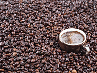A brown cup with aromatic espresso stands in the coffee beans. Roasted coffee beans, background. Horizontal orientation. Fresh aromatic dark coffee. Close-up. Selective focus on a cup with espresso.