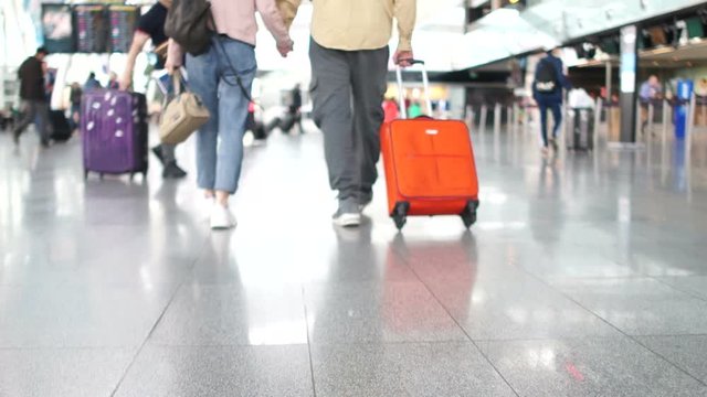 Close-up of the legs of a man and woman at the airport. Husband and wife walk around the train station and carry a bright orange suitcase