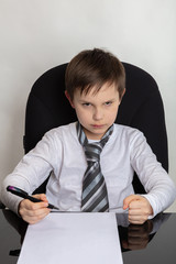 Close up of a cute brunette boy Presents being a director. The boy writes a letter In a white T-shirt, a man’s tie on his head