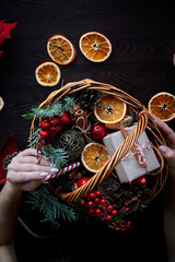 Wicker basket with striped candy canes, dried sliced oranges, cones and gifts. Cozy atmosphere at home before Christmas. Rustic basket with green spruce branches and gifts in craft paper.
