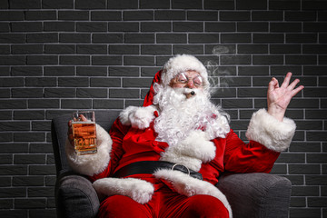 Funny drunk Santa Claus showing OK while sitting in armchair against brick background