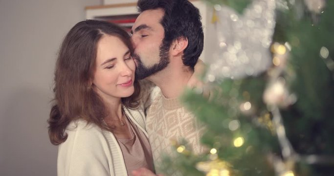 Romantic couple decorating Christmas tree. Slow dance, kisses and sweet embrace. Concept of Love, Young Family, Holidays and Romance.