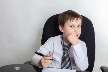 Close up of a cute brunette boy Presents being a director. The boy writes a letter In a white...