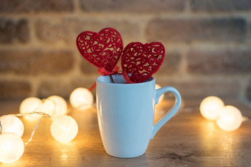 White Mug Mock Up with Two Red Hearts. Valentines Day Concept. Brick Background and Lights