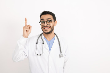 Fototapeta premium Young smiling therapeutist in whitecoat and eyeglasses pointing upwards