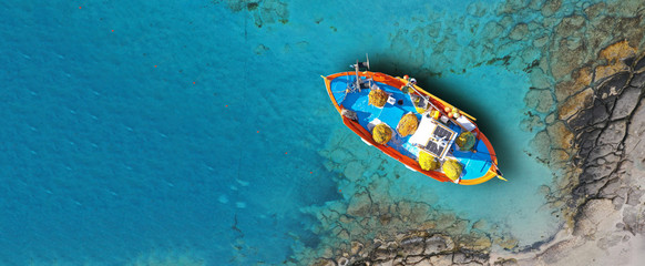 Aerial drone top down ultra wide photo of traditional fishing boat docked in world famous paradise beach of Mykonos island, Cyclades, Greece