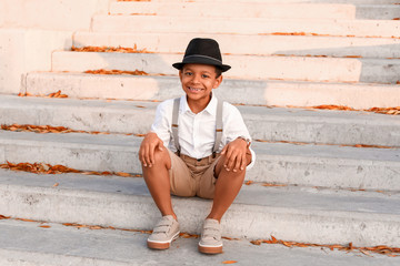 Cute fashionable African-American boy sitting on stairs outdoors