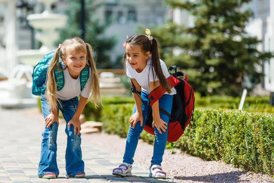 two little schoolgirls with heavy backpacks go to school