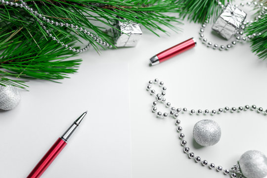 Christmas holiday background - decoration on a white table background with blank white sheet and red pen. New year pine and silver Christmas balls. Top view. Place for text.