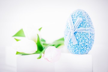 Happy Easter. Blue Easter egg and delicate tulips on a white background. Copy space