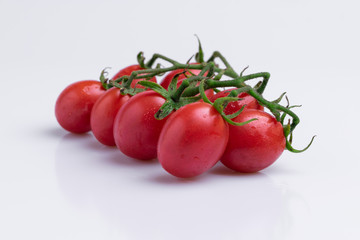 Grape or cherry tomato branch. Pile of red grape tomatoes isolated on white background, soft light, angle view, studio shot.