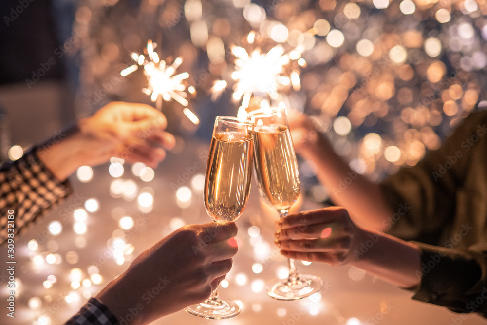 Wall mural hands of couple with flutes of champagne and their friends with bengal lights