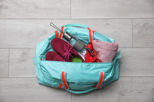 Sports bag with gym stuff on wooden floor, top view