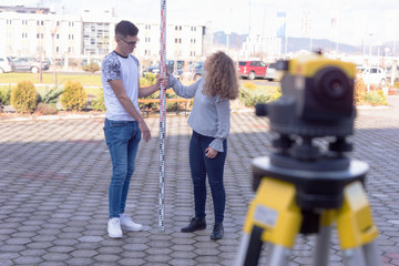 Two students of architecture doing practice lessons as  Surveyor Engineering. Surveyor&rsquo;s telescope at construction site for making contour plans of the land before startup construction work.