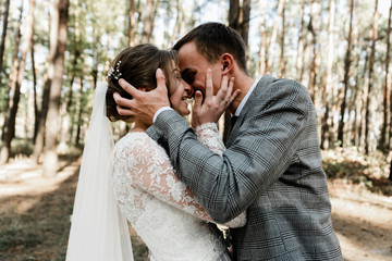 Attractive couple celebrating their wedding in forest. Portrait of young happy groom and bride in wedding clothes standing together, holding hands and looking at each other