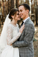 Attractive couple celebrating their wedding in forest. Portrait of young happy groom and bride in wedding clothes standing together, holding hands and looking at each other